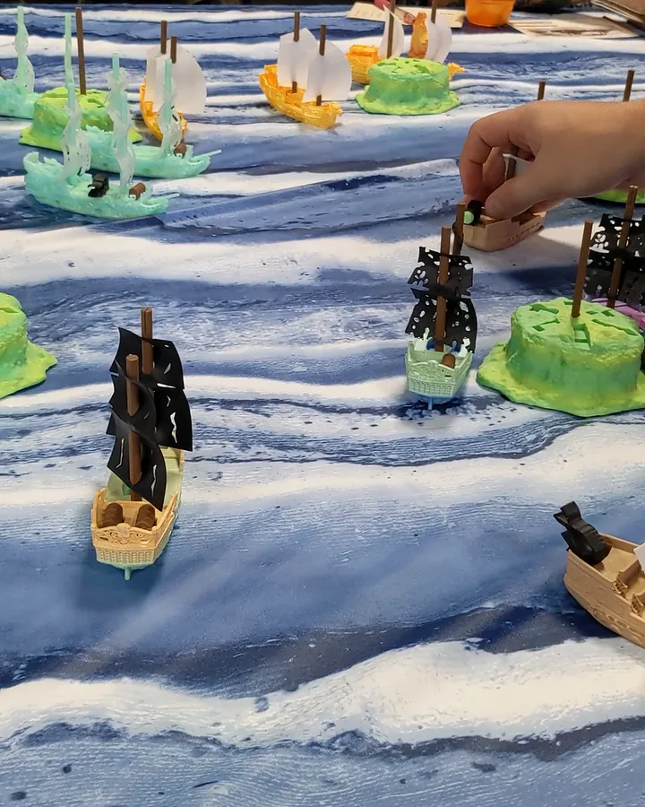 A player loads a cannon while fleets sail past the islands.